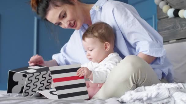 年轻的母亲和婴孩在卧室看图画书 — 图库视频影像