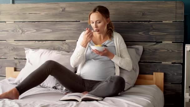 Zwangere Vrouw Eten Het Lezen Van Een Boek Slaapkamer — Stockvideo