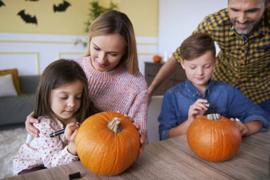 Çocuklar ve ebeveynler balkabağı çiziyor.