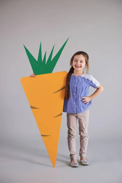 微笑的女孩拿着一个大的 人造胡萝卜在演播室拍摄 — 图库照片