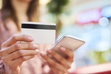 Çevrimiçi alışveriş sırasında cep telefonu ve kredi kartı kullanan kadın 