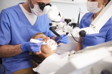Diş hekimi mikroskobu kullanarak ve kadın dişlerini muayene