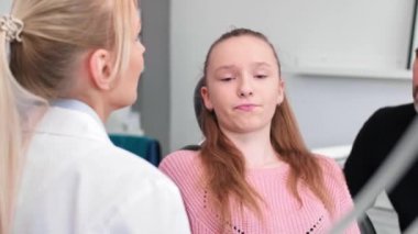 Dişçi, genç kız ve babasıyla dişçi kliniğinde konuşuyor