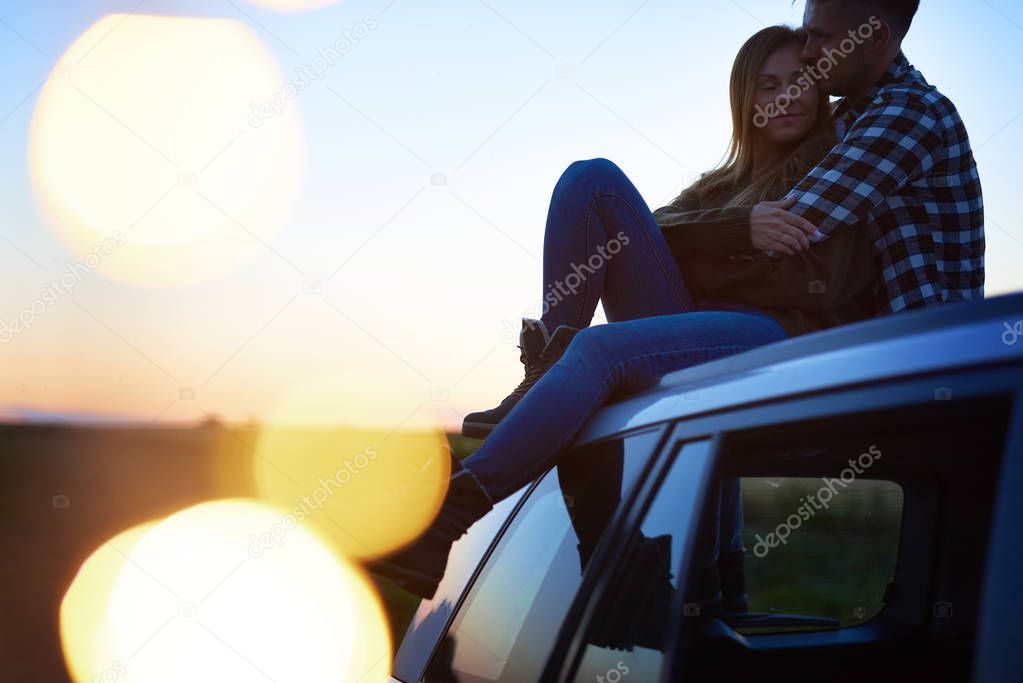 Loving couple embracing and sitting on car 
