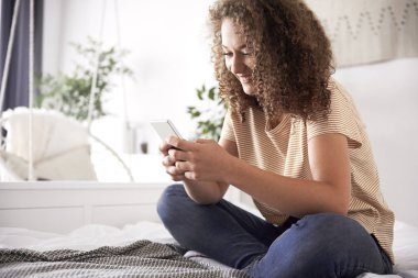 Genç kız yatakta bir cep telefonu kullanarak 