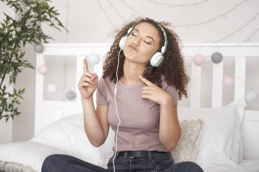 Joyful girl listening to music and dancing on the bed 