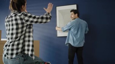 Duvara resim çerçevesi asan bir çiftin videosu. 8K 'da kırmızı helyum kamerayla çekildi.