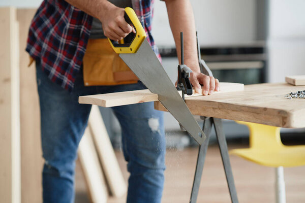  Man cutting block of wood using hand saw                              