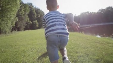 Arka planda çimlerin üzerinde oynayan bir çocuğun videosu var. 8K 'da kırmızı helyum kamerayla çekildi.. 