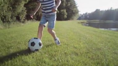 Küçük çocuğun çimlerin üzerinde futbol oynadığı videoyu izliyorum. 8K 'da kırmızı helyum kamerayla çekildi.