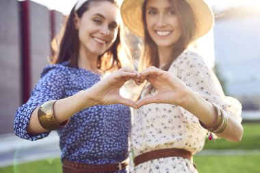 İki gülümseyen kadın bir elden kalp yapıyor.                               