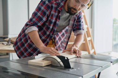 Koruyucu gözlüklü marangoz dairesel testere ile kesiyor.                               