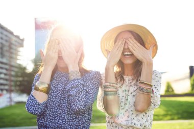 İki mutlu genç kadın elleriyle gözlerini kapatıyor.                                