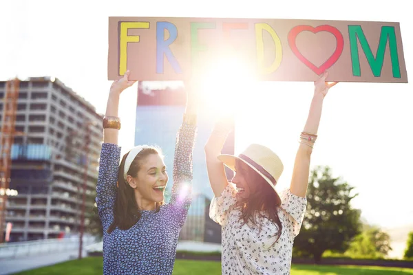 Duas Mulheres Felizes Com Cartaz Cores Olhando Para Mesmo — Fotografia de Stock