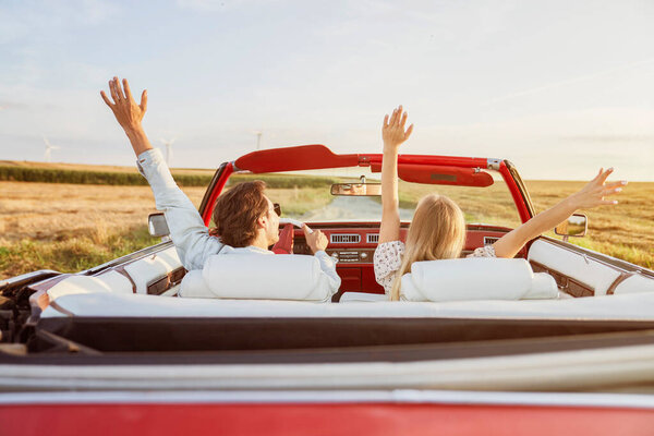 Rear view of couple driving in convertible under sunny sky                               