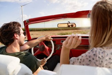 Tarlalar ve yel değirmenleri arasında araba süren çiftin dikiz görüntüsü                               