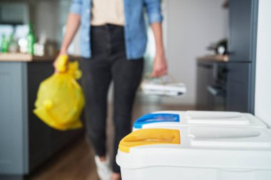 Sarı plastik çantalı bir kadın çöp kutusuna gidiyor.