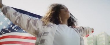Şehirde Amerikan bayrağı taşıyan genç bir kadının videosu. 8K 'da kırmızı helyum kamerayla çekildi..