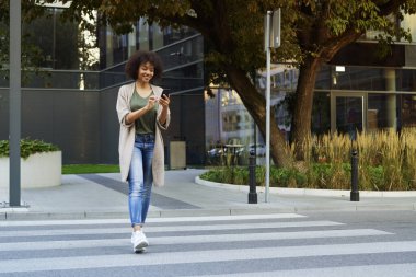 Cep telefonlu bir kadın karşıdan karşıya geçiyor.