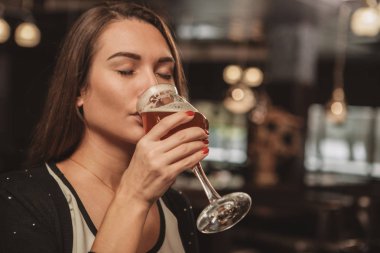 Çok güzel bir genç kadının restoranda lezzetli bira içme zevk kapatın. Güzel kadın gözleri ile cam lezzetli zanaat bira yudumlarken pleasure kapalı. Gevşeme, hafta sonu kavramı