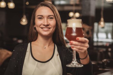 Bardak zanaat bira için kamera, yerel barda rahatlatıcı mutlu bir şekilde uzatarak gülümseyen sevimli güzel kadın. Muhteşem kadın müşteri ile onun bira cam toasting. Oktoberfest, parti konsept