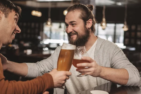 Cheerful bearded man telling jokes to his friend over a glass of beer at local irish pub. Happy man enjoying drinking beer with his brother. Two male friends celebrating at the bar. Friendship concept