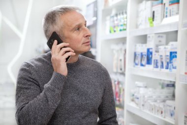 Eczanede alışveriş yaparken onun akıllı telefon kullanan olgun adam. Onun doktor talimatı diyor ilaçları eczaneden, satın alma kıdemli erkek müşteri. Tüketim, teknoloji, mobilite kavramı
