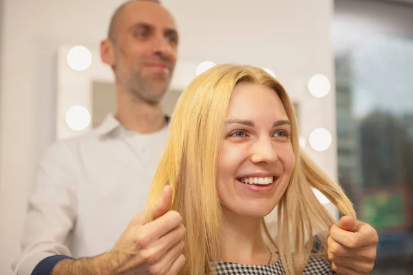 Close up of a happy woman laughing, talking to her hairstylist while getting new hairdo. Cheerful young female at hair salon. Professional hairdresser working with his client. Communication, service concept