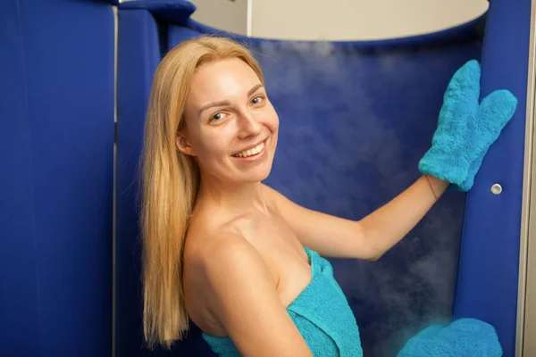 Cryotheraby sauna kabini girerek onun omuz üzerinden kameraya gülümseyen neşeli genç sarışın saçlı bir kadın. Tam vücut kriyoterapi yordam Güzellik Salonu için çekici kadın