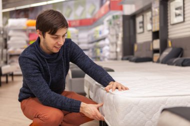 Ortopedik yatak mobilya mağazasında, kopya alanı inceleyerek yakışıklı neşeli adam. Yeni yatak satın almak seçerek genç adam evde mobilya bölümü, alışveriş. Dinlenme, rahatlama, sağlık kavramı