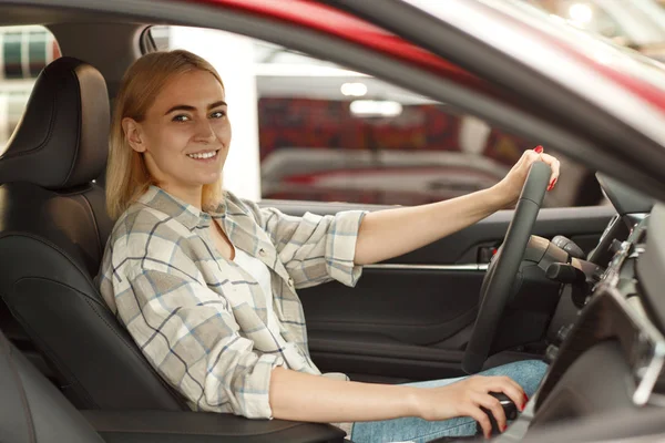 美丽的女司机微笑着对着坐在经销商沙龙的一辆新汽车的相机微笑 快乐有吸引力的女人选择新车 购买汽车的女客户 消费主义 安全理念 — 图库照片