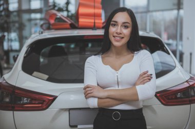 Onun yeni araba Bayilik salonu yakınındaki gururla poz kameraya gülümseyen güzel mutlu uzun saçlı bir kadın. Çatıda bir kırmızı yay ile yeni otomobil kazanan muhteşem bir kadın. Arabalar kavramı