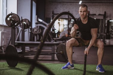 Yakışıklı kaslı crossfit atlet spor stüdyosu, kopya alanı egzersiz. Erkek atlet fonksiyonel eğitim salonunda savaş halatlar ile çalışma dışarı içinde. Kardiyo, hareket, sağlıklı yaşam konsepti