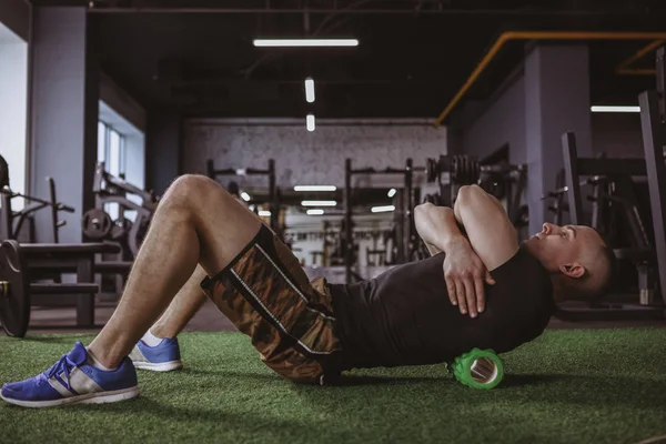 Tam uzunlukta bir erkek atlet spor salonunda çalışma dışarı sonra köpük rulo kullanarak bir kadeh. Masaj ve köpük rulo onun sırt kasları germe sporcu. Sağlık, kabartma, yaralanma kavramı