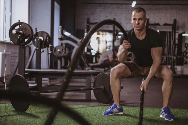Yakışıklı kaslı crossfit atlet spor stüdyosu, kopya alanı egzersiz. Erkek atlet fonksiyonel eğitim salonunda savaş halatlar ile çalışma dışarı içinde. Kardiyo, hareket, sağlıklı yaşam konsepti