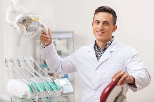 Cheerful male dentist smiling joyfully at his dental office, copy space. Attractive male professional dentist posing proudly at his clinic. Experienced doctor at his workplace. Confidence, success
