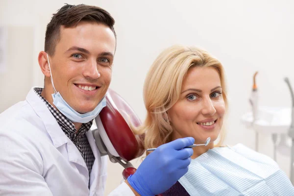幸せな男性歯科医と彼の成熟したメスの患者歯科検診後カメラに嬉しそうに笑顔します 歯科医を訪問健康な白い歯と美しい女性 歯科医療コンセプト — ストック写真