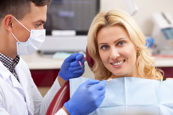Beautiful happy mature woman with healthy perfect teeth smiling, sitting at the dental chair. Attractive female patient smiling joyfully during teeth examination by professional dentist. Dentistry