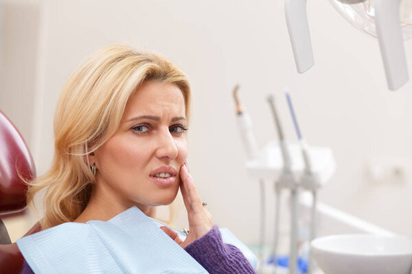 Close up of a beautiful mature woman looking exhausted suffering from toothache, copy space. Female patient with painful teeth issues looking to the camera while waiting for her dentist 