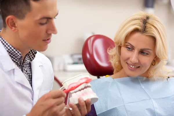 Male dentist showing his female patient how to brush teeth correctly, using dental mold. Mature woman watching her dentist explaining about teeth and gums care. Dentistry, perfect teeth concept