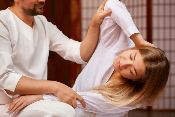 Young woman stretching her body with the help of professional thai massage therapist at spa center. Male masseur performing thai massage on his client. Recreation, relaxation, healing concept