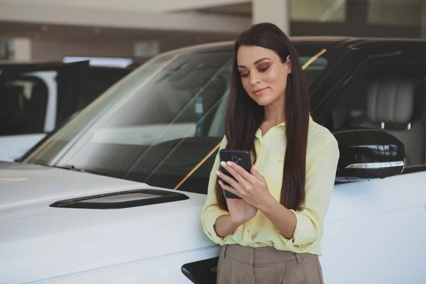 Donna attraente utilizzando il suo smartphone mentre bying nuova auto — Foto Stock