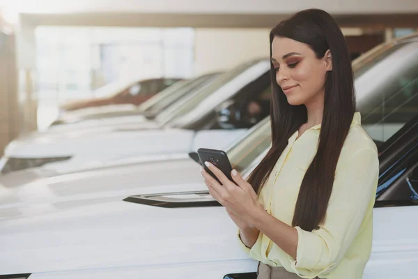 Mulher atraente usando seu telefone inteligente enquanto bying carro novo — Fotografia de Stock