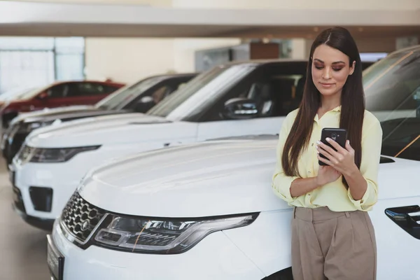 Mulher atraente usando seu telefone inteligente enquanto bying carro novo — Fotografia de Stock
