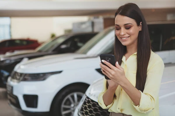 Donna attraente utilizzando il suo smartphone mentre bying nuova auto — Foto Stock