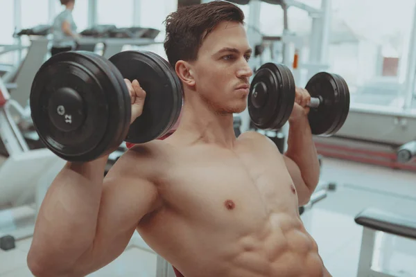 Hombre sin camisa rasgado haciendo ejercicio con pesas en el gimnasio — Foto de Stock