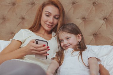 Beautiful woman and her little daughter using smart phone
