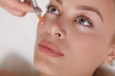 Güzel bir kadının kozmetoloji kliniğinde yüz doldurma iğnesi yaptırırken yakın plan çekimleri.