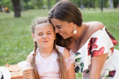 Şirin bir genç kız komik surat yapıyor, parkta annesine sarılıyor.