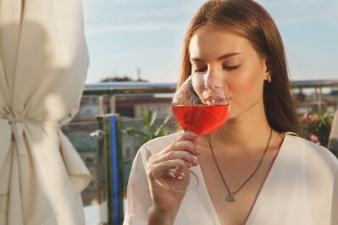 Gün batımında bar terasında gül içen güzel bir kadını yakından çek.